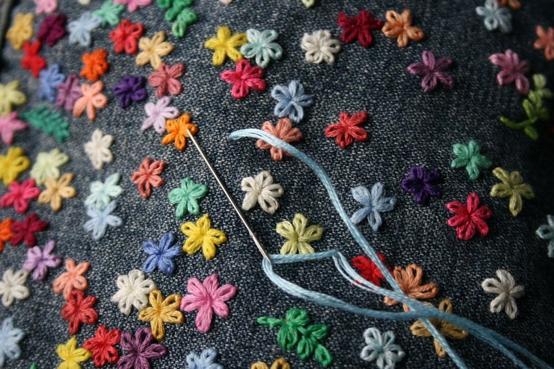 Nål och blå tråd över mörkt tyg med färgglada broderade blommor